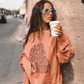 Model wearing Kinga Csilla Abracadabra OG Jumper in warm orange with oversized fit and graphic print, styled street-side with coffee cup and sunglasses