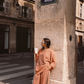 Model wearing Kinga Csilla Abracadabra OG Jumper in terracotta orange with wide-leg Abracadabra  Hades Pants, styled on Rue de Rivoli in Paris with oversized streetwear look and coffee cup