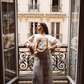 Woman standing on a Parisian balcony in the Kinga Csilla Shell OG Jumper cream oversized sweater, styled with a white lace maxi skirt for a relaxed bohemian outfit.