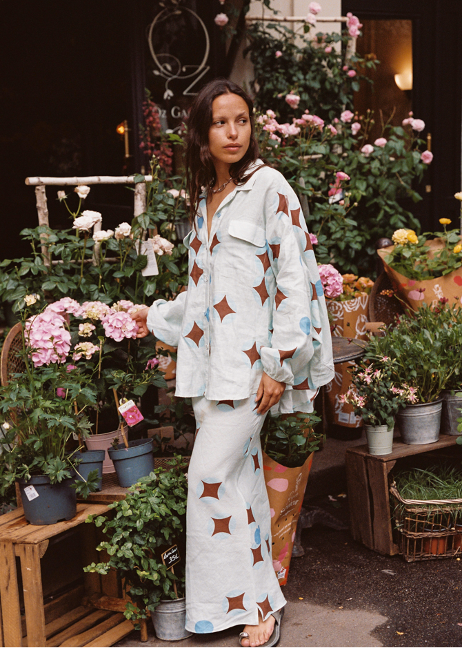 Model wearing Kinga Csilla Aquarius Chalm Shirt in celestial linen with matching Aquarius Column Skirt, styled among fresh flowers outside a Paris florist