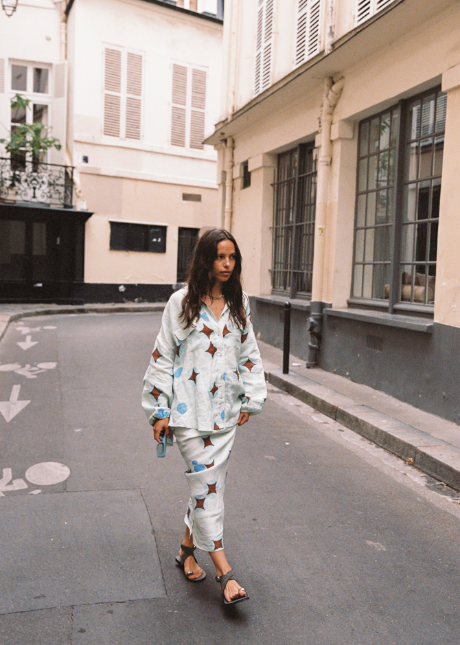 Model wearing Kinga Csilla Aquarius Chalm Shirt in celestial baby blue linen with matching Aquarius Column Skirt, styled as a coordinated set with sandals and blue sunglasses in a Parisian street
