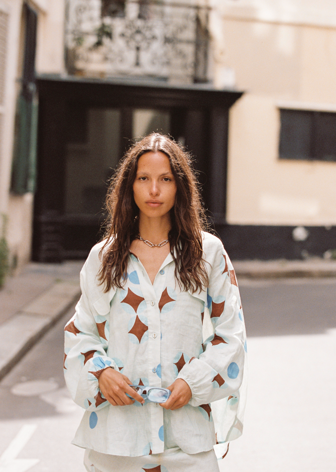 Close-up of model wearing Kinga Csilla Aquarius Chalm Shirt in light linen with celestial-inspired geometric print, styled with loose waves and sunglasses in hand