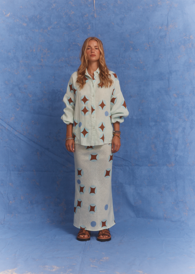 Model wearing Kinga Csilla Aquarius Chalm Shirt and matching Aquarius Chalm Skirt set in linen, photographed against a blue studio backdrop