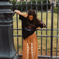 Model in Kinga Csilla Bello Swirl Jessi Pant with white embroidery, styled with oversized Kinga Csilla Sunset tee, leaning against Paris fence in casual street style setting