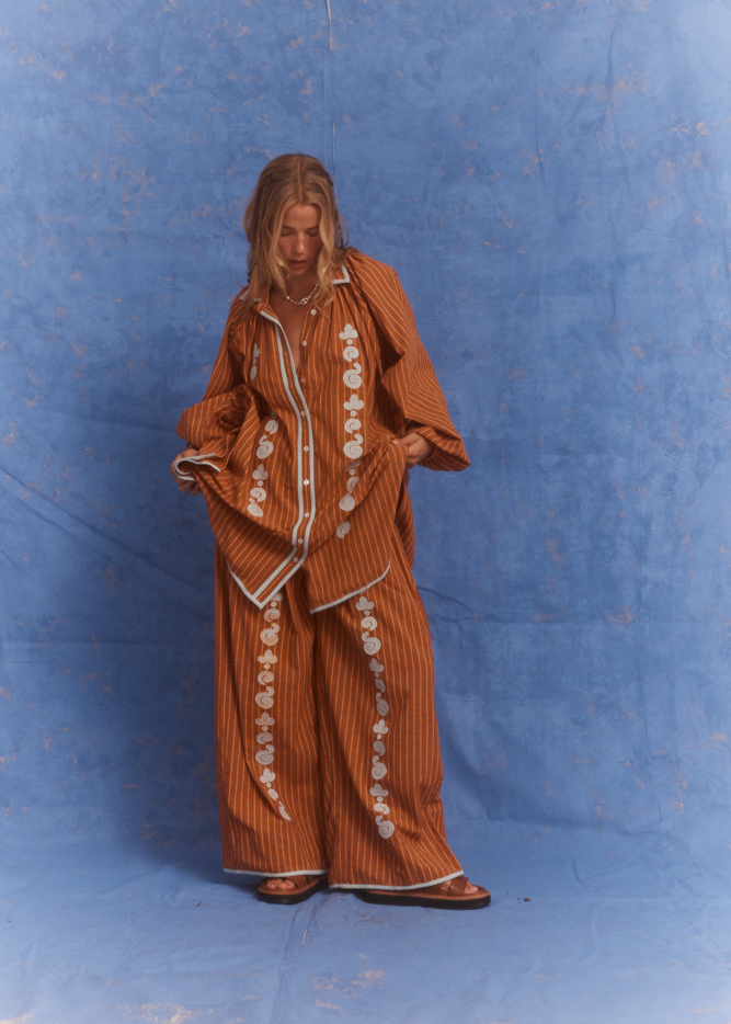 Model wearing Kinga Csilla Bello Swirl Jessi Pant with matching Bello Swirl Cup Shirt Dress in burnt orange with embroidered white swirl detailing, styled as a coordinated set