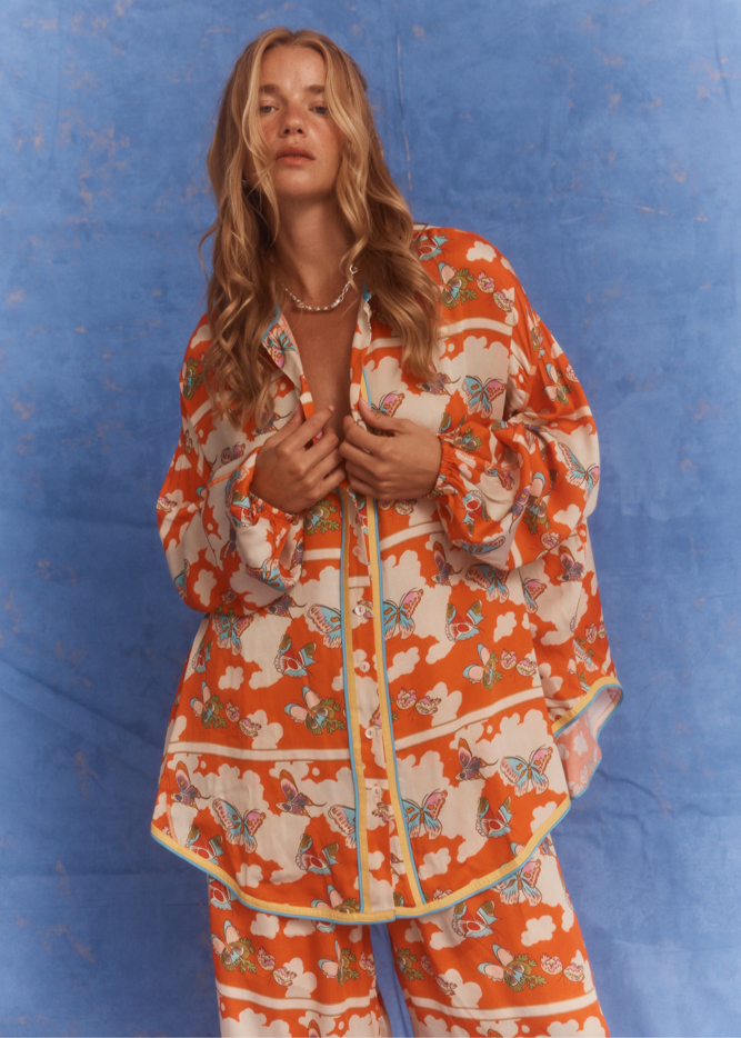 Close-up of model wearing Kinga Csilla Farfalla Chalm Shirt and Farfalla Jessi Pant in vibrant orange butterfly print co-ord set