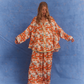 Model wearing Kinga Csilla Farfalla Chalm Shirt and Jessi Pant in oversized orange butterfly print co-ord set against blue backdrop