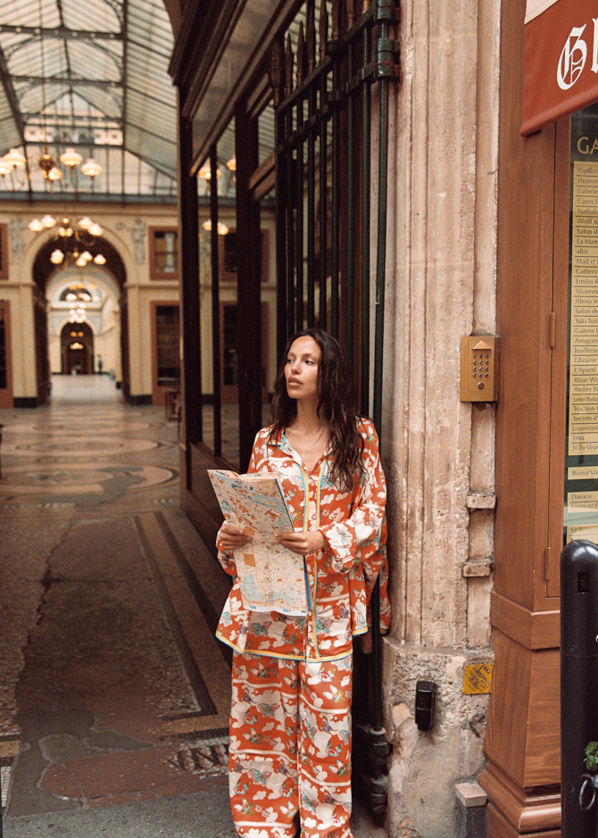 Model wearing Kinga Csilla Farfalla Chalm Shirt and Jessi Pant in orange butterfly print, oversized co-ord set styled with city map for Paris travel outfit