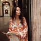 Model wearing the Kinga Csilla Farfalla Chalm Shirt in orange butterfly print, styled with matching Farfalla Jessi Pant, holding a map in a Paris arcade.