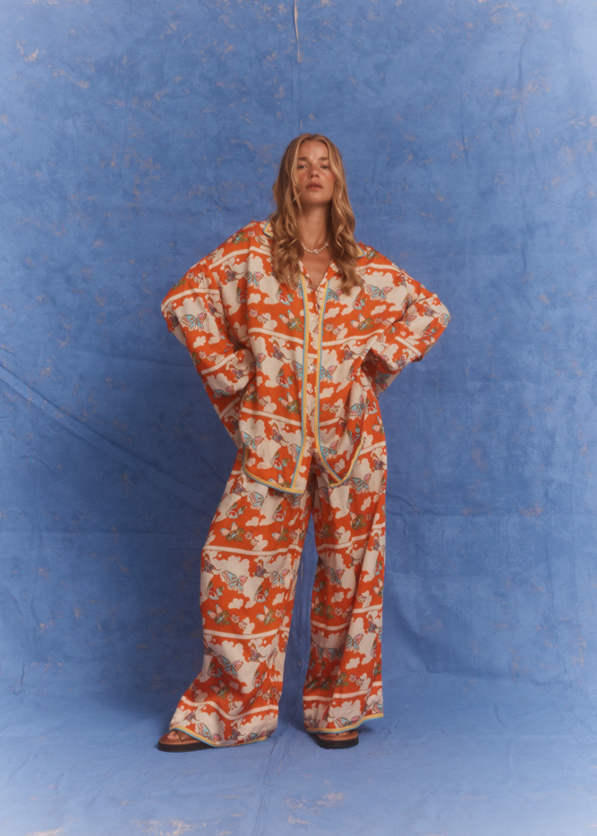Kinga Csilla Farfalla Jessi Pant – relaxed wide-leg orange butterfly print pant with elasticated waist and silky drape, styled with the matching Farfalla Chalm Shirt, women’s statement fashion set on blue backdrop.