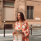 Model in Kinga Csilla Farfalla Jessi Pant with matching Farfalla Chalm Shirt, orange butterfly print set, holding a map while standing on a Paris street.