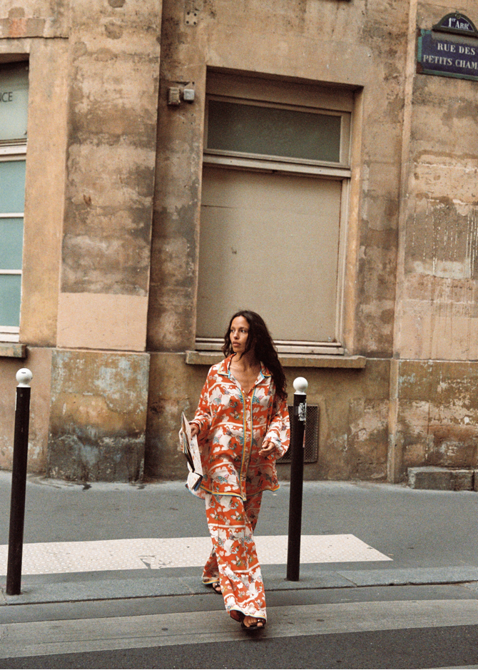 Model walking on a Paris street in Kinga Csilla Farfalla Jessi Pant with matching Farfalla Chalm Shirt, bold orange butterfly print set, holding a folded map.