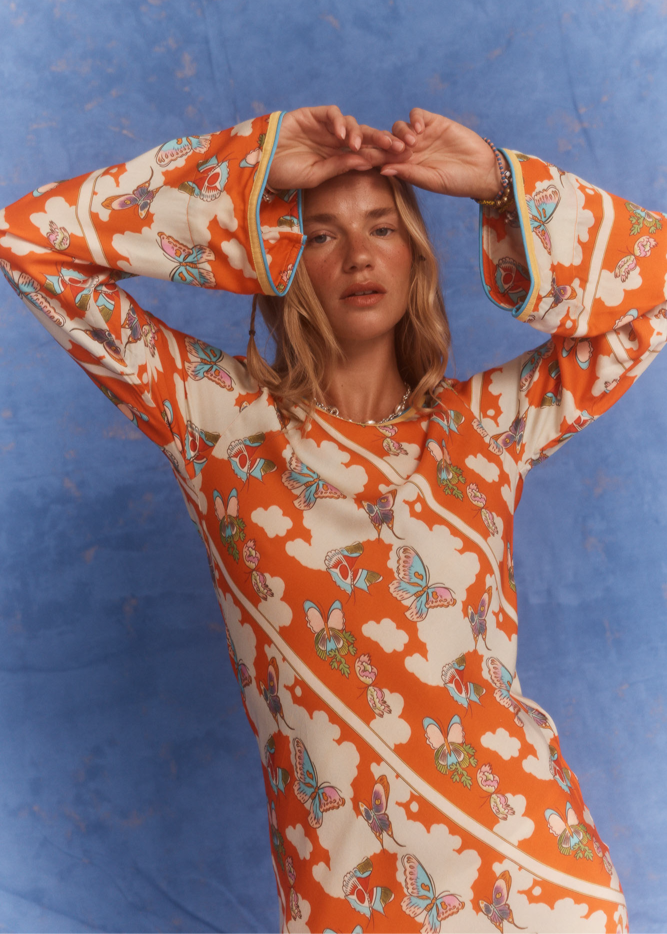 Close-up of the Kinga Csilla Farfalla Olive Dress in studio, highlighting the vivid orange butterfly and cloud print with flared sleeves and contrast trim.