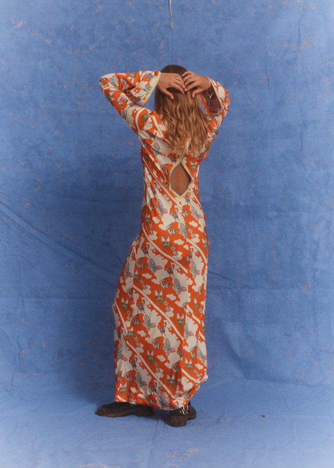 Back view of the Kinga Csilla Farfalla Olive Dress in studio, featuring its bold orange floral and butterfly print and diamond-shaped keyhole cut-out detail.