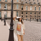 Model wearing Kinga Csilla Hibiscus Tee with bold hibiscus print, styled with TWILIGHT VELVET FLARE PANT, standing on Paris bridge with newspaper in hand
