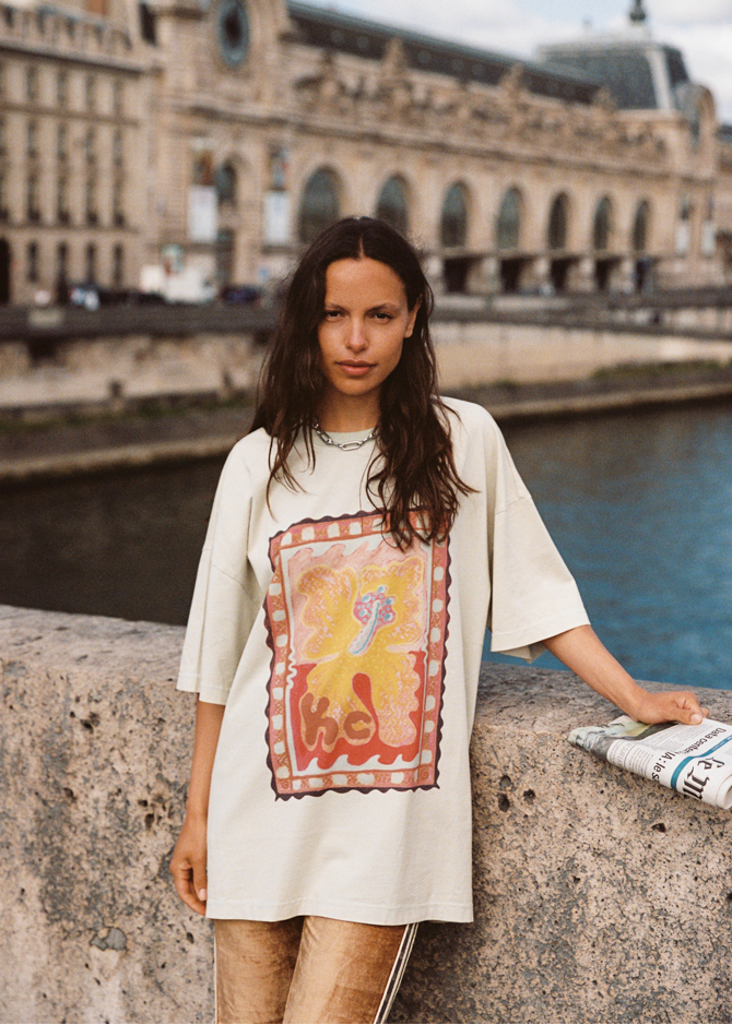 Model wearing Kinga Csilla Hibiscus Tee with oversized fit and stamp-style hibiscus print, photographed riverside in Paris
