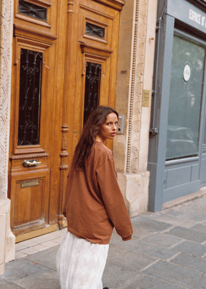Close back view of model wearing Kinga Csilla Lino Roses Tee in brown, oversized long sleeve styled with Tottori Lace Ode Skirt, outdoor street scene