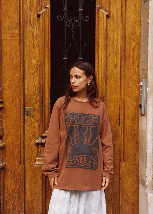 Model wearing Kinga Csilla Lino Roses Tee in brown, oversized long sleeve with vintage lino graphic, styled with Tottori Lace Ode Skirt in front of door.