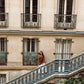 Full outfit shot of model in Kinga Csilla Lino Roses Tee brown long sleeve, styled with Tottori Lace Ode Skirt, standing on Parisian stone staircase with architectural building backdrop
