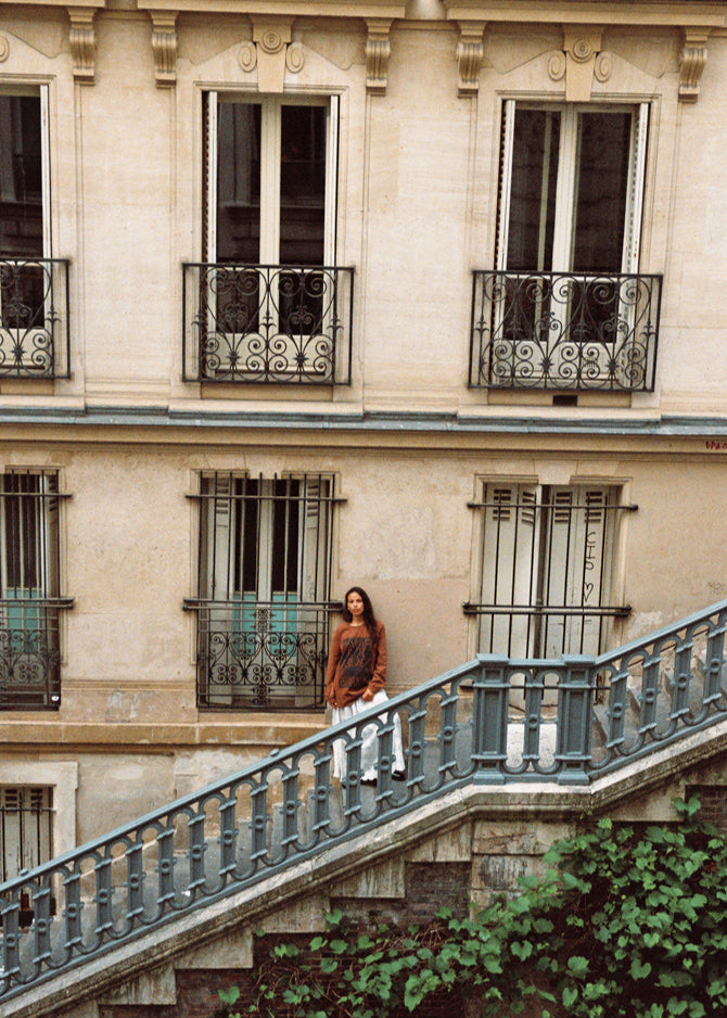 Full outfit shot of model in Kinga Csilla Lino Roses Tee brown long sleeve, styled with Tottori Lace Ode Skirt, standing on Parisian stone staircase with architectural building backdrop