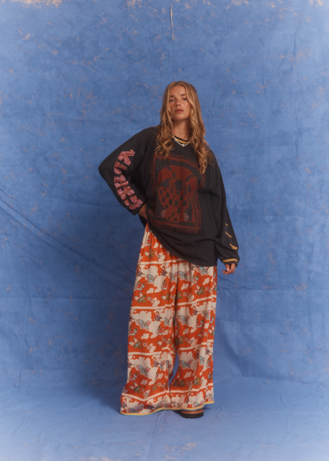 Model in Kinga Csilla Love Potion Roses Tee stonewashed black with graphic rose print, styled with Farfalla Jessi Pant in orange butterfly cloud motif.
