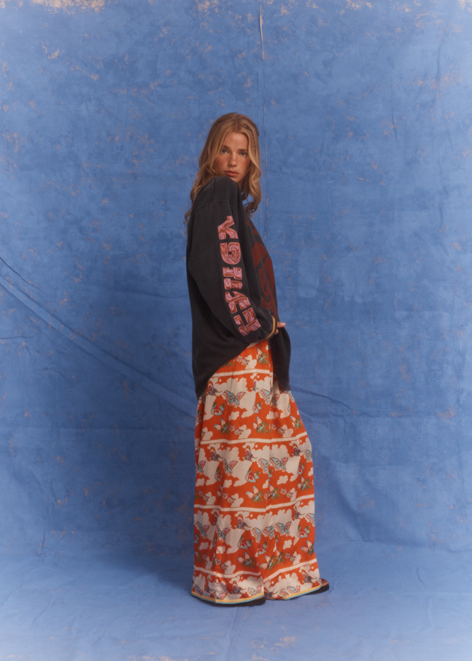 Model wearing Kinga Csilla Love Potion Roses Tee in stonewashed black with mystical rose artwork, styled with Farfalla Jessi Pant in bold orange butterfly print