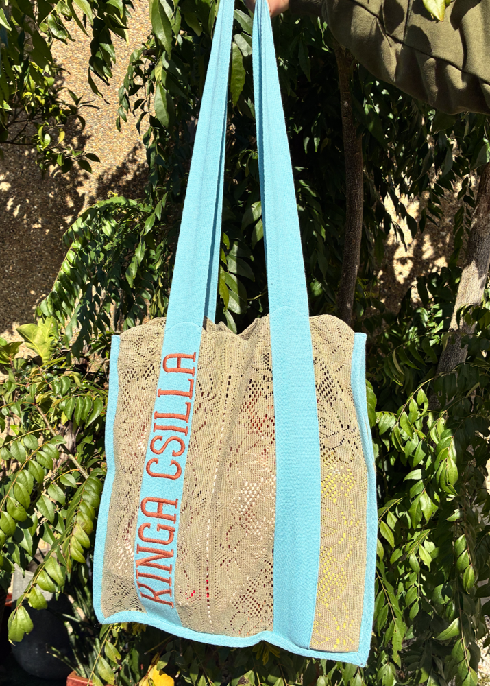 Front view of Kinga Csilla Rainy Lace KC Shoulder Bag with aqua blue straps and logo embroidery, featuring intricate sage lace body, lightweight artisanal tote.