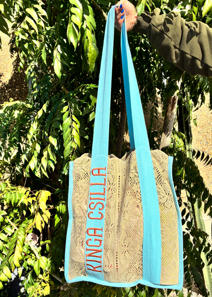 Kinga Csilla Rainy Lace KC Shoulder Bag held by model outdoors, featuring aqua blue straps, bold logo embroidery, and sage lace body design.