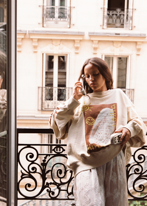 Kinga Csilla Shell OG Jumper in cream, oversized sweatshirt with shell and sun graphic, boho coastal-inspired sweater styled with lace pants on balcony, relaxed slouchy fit.