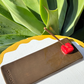 Handcrafted Kinga Csilla x Staycay ceramic incense holder in earthy brown with a glossy red cube incense rest. Unique bohemian artisan incense tray for home décor, meditation, and aromatherapy. Styled outdoors on a white scalloped table with lush green succulent backdrop.