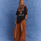 Studio shot of model wearing Kinga Csilla Sunset Tee in black with sun logo, paired with Bello Swirl Jessi Pants featuring floral embroidery, against a blue backdrop