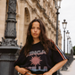 Model wearing Kinga Csilla Sunset Tee in black cotton with graphic sun print and striped sleeves, styled with Bello Swirl Jessi Pant  in a street-style setting