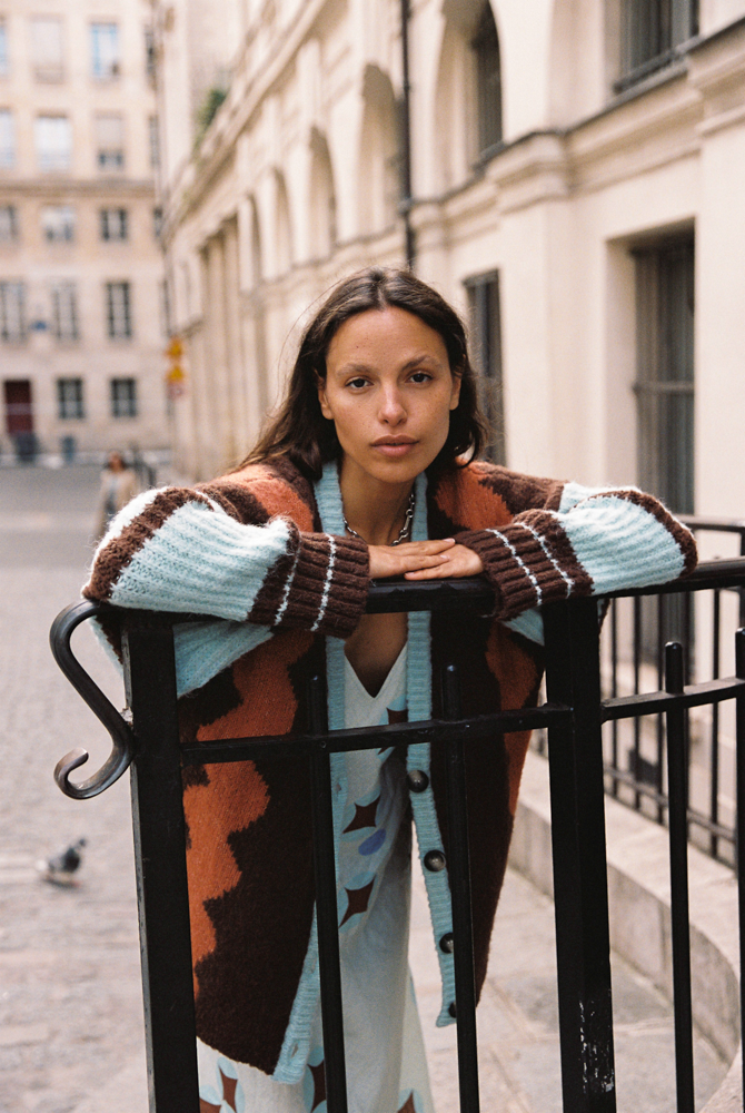 Close-up of model wearing the Kinga Csilla Surf Citta Cardigan in brown, orange and light blue stripes — oversized knit styled over Aquarius Slip Dress  in a European street scene.