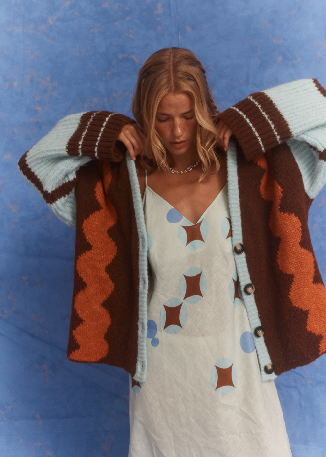 Model wearing the Kinga Csilla Surf Citta Cardigan, a bohemian-inspired knit in brown, orange and blue, layered over the Aquarius Slip Dress.