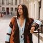 Model wearing the Kinga Csilla Surf Citta Cardigan in brown, orange and baby blue — oversized chunky knit styled over a Aquarius Slip Dress, shot in a European street setting.