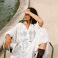Woman wearing the Kinga Csilla Tottori Lace Harlow Maxi Dress in sheer white embroidered cotton, button-down style with scalloped hem, styled with boots while reading by the fountain.