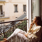 Model in Kinga Csilla Tottori Lace Ode Skirt, white lace maxi skirt styled with oversized graphic Shell Og Jumper, relaxing on Paris balcony with coffee cup