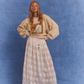 Model wearing Kinga Csilla Tottori Lace Ode Skirt, white lace maxi skirt styled with oversized beige Shell OG Jumper, studio photoshoot on blue backdrop