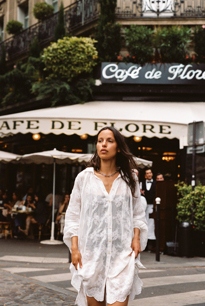 Woman in Kinga Csilla Tottori Lace Pia Mini white lace dress walking in front of Café de Flore in Paris, effortless French summer outfit inspiration.