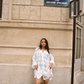 Woman wearing the Kinga Csilla Tottori Lace Pia Mini in white cotton lace, styled with embroidery and scalloped hem, photographed in Paris street.
