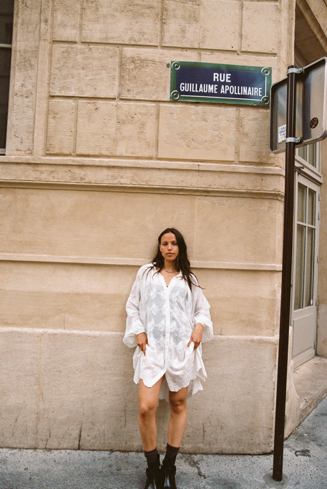 Woman wearing the Kinga Csilla Tottori Lace Pia Mini in white cotton lace, styled with embroidery and scalloped hem, photographed in Paris street.