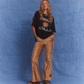Model wearing Kinga Csilla Twilight Velvet Flare Pant in golden velvet with KC logo stripe, styled with oversized Kinga Csilla Sunset tee, photographed against a blue studio backdrop.