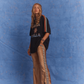 Model wearing Kinga Csilla Twilight Velvet Flare Pant in golden velvet with black logo side stripe detail, styled with oversized Kinga Csilla Sunset tee, photographed against a blue studio backdrop.