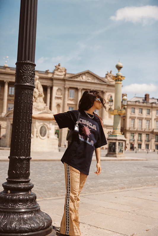 Model wearing Kinga Csilla Twilight Velvet Flare Pant in golden stretch velvet with KC logo piping, styled with oversized Kinga Csilla Sunset tee, photographed in a Paris street setting.