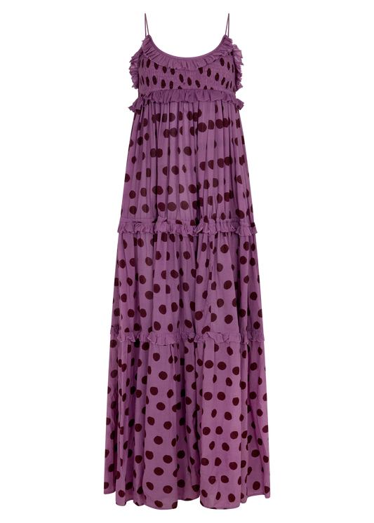 A tiered maxi dress in a dusty purple color with dark brown polka dots, featuring thin spaghetti straps and ruffled trim along the neckline and between the tiers, shown against a plain white background.