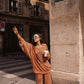 Woman in an orange tracksuit set standing on a street corner in Paris, holding a coffee cup.