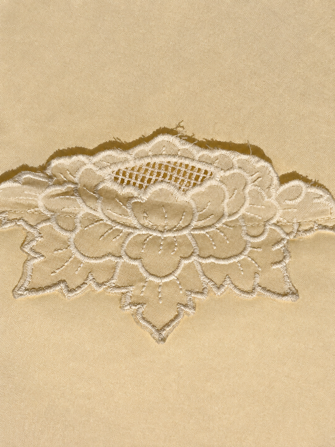 A close-up of a cream embroidered lace applique with a floral pattern, laid flat on a matching beige textured background.