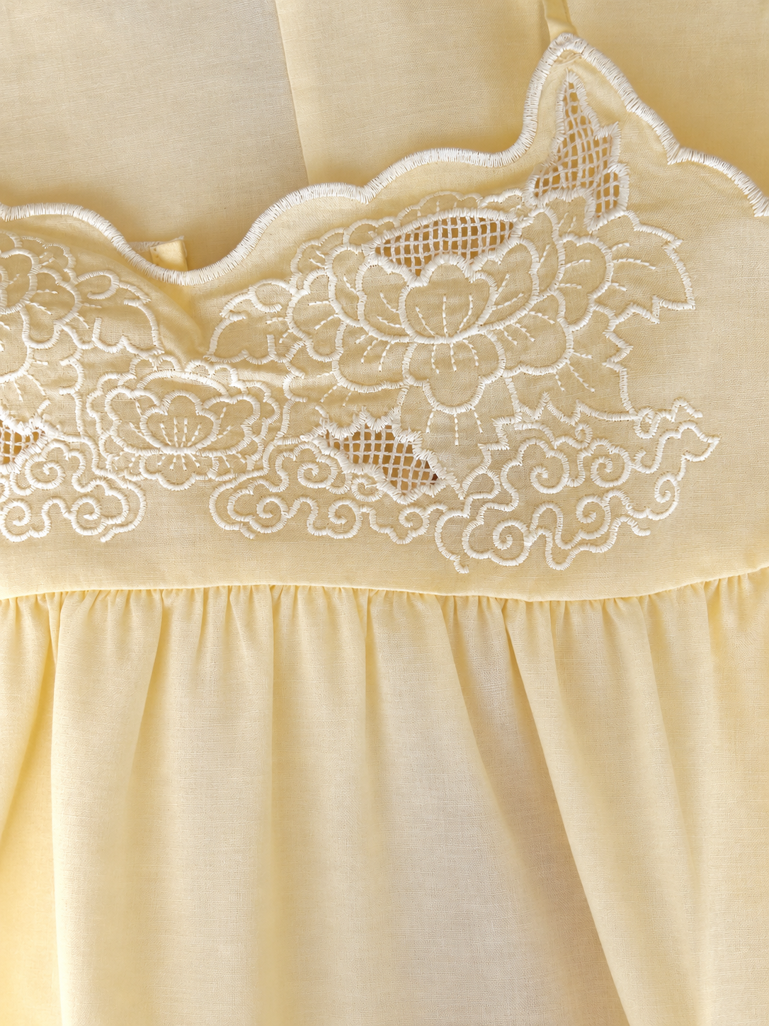 Close-up of a cream-colored fabric garment with white floral embroidery and a scalloped embroidered neckline.