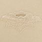 A close-up of a cream colored fabric surface featuring a delicate white floral lace applique patch.