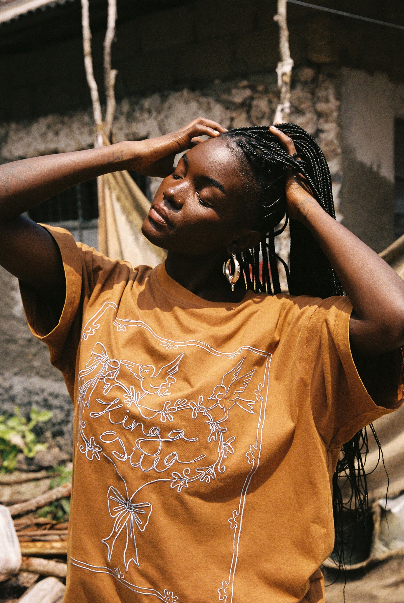 Woman wearing a brown oversized t-shirt with baby blue graphics and text, standing outdoors.
